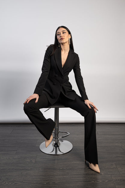Tailleur doppiopetto nero da cerimonia, giacca strutturata e pantalone palazzo indossato in posa seduta