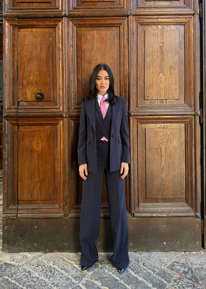 tailleur blu navy con giacca monopetto sfiancata, gilet e pantaloni, donna davanti a portone in legno.