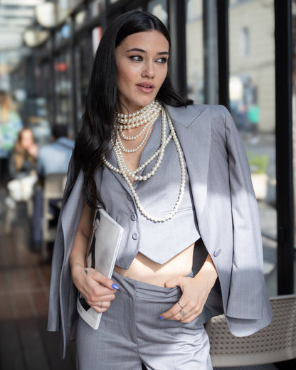 Modella in ARES GESSATO: tre pezzi, giacca oversize monopetto, gilet crop e pantaloni palazzo con collane di perle.